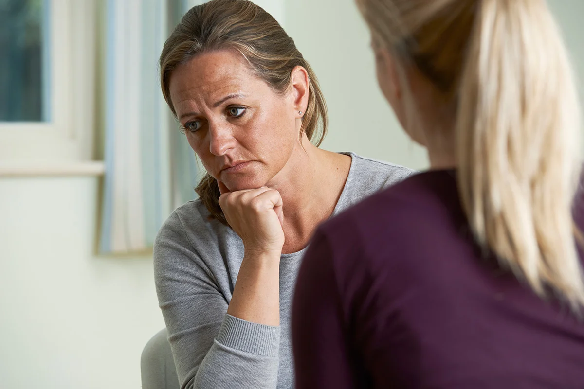 A woman sits with her chin on her hand, listening thoughtfully during a counseling session.