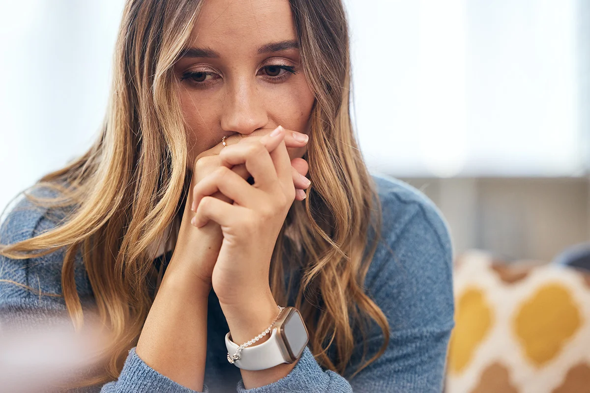A woman sits quietly, resting her chin on her hands, appearing deep in thought.