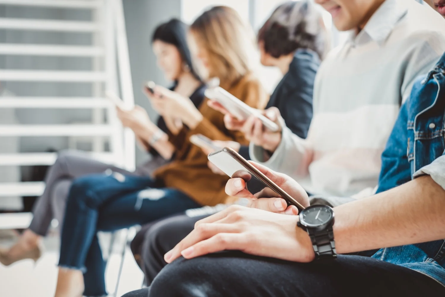 Group of people sitting in a row using smartphones, all focused on their screens, representing technology use, social media engagement, or digital communication.
